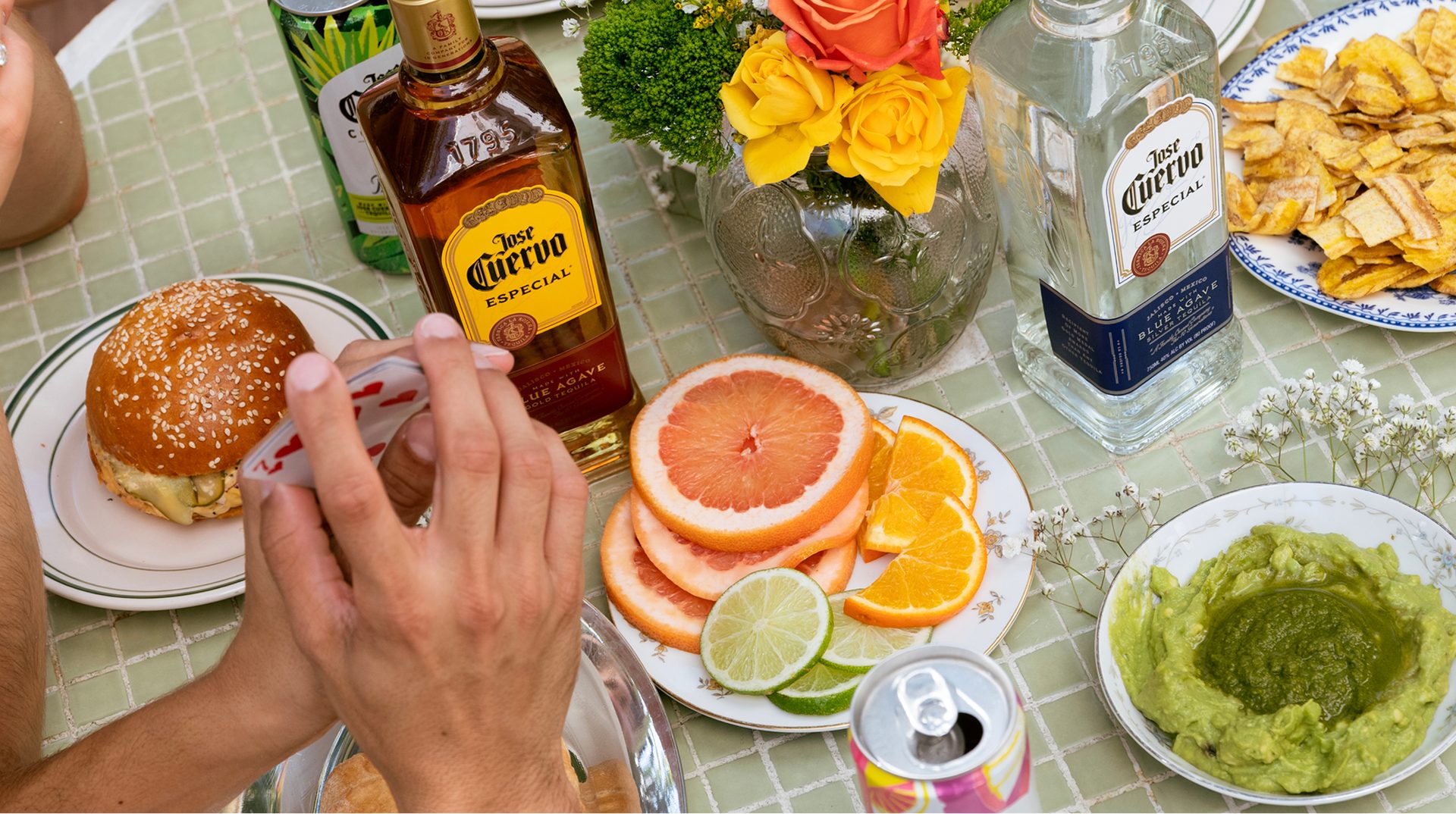 Overhead view of a margarita bar spread with Jose Cuervo Especial Gold and Silver bottles, sliced citrus, guacamole and plantain chips